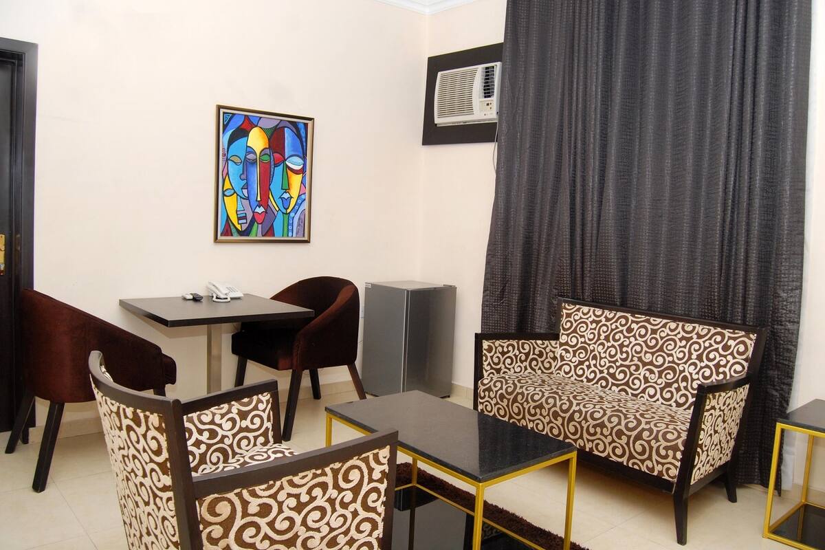 A room with a dining table, two chairs, a sofa, a small table, and a painting on the wall.