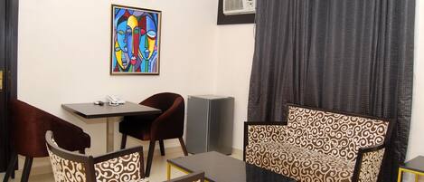 A room with a dining table, two chairs, a sofa, a small table, and a painting on the wall.