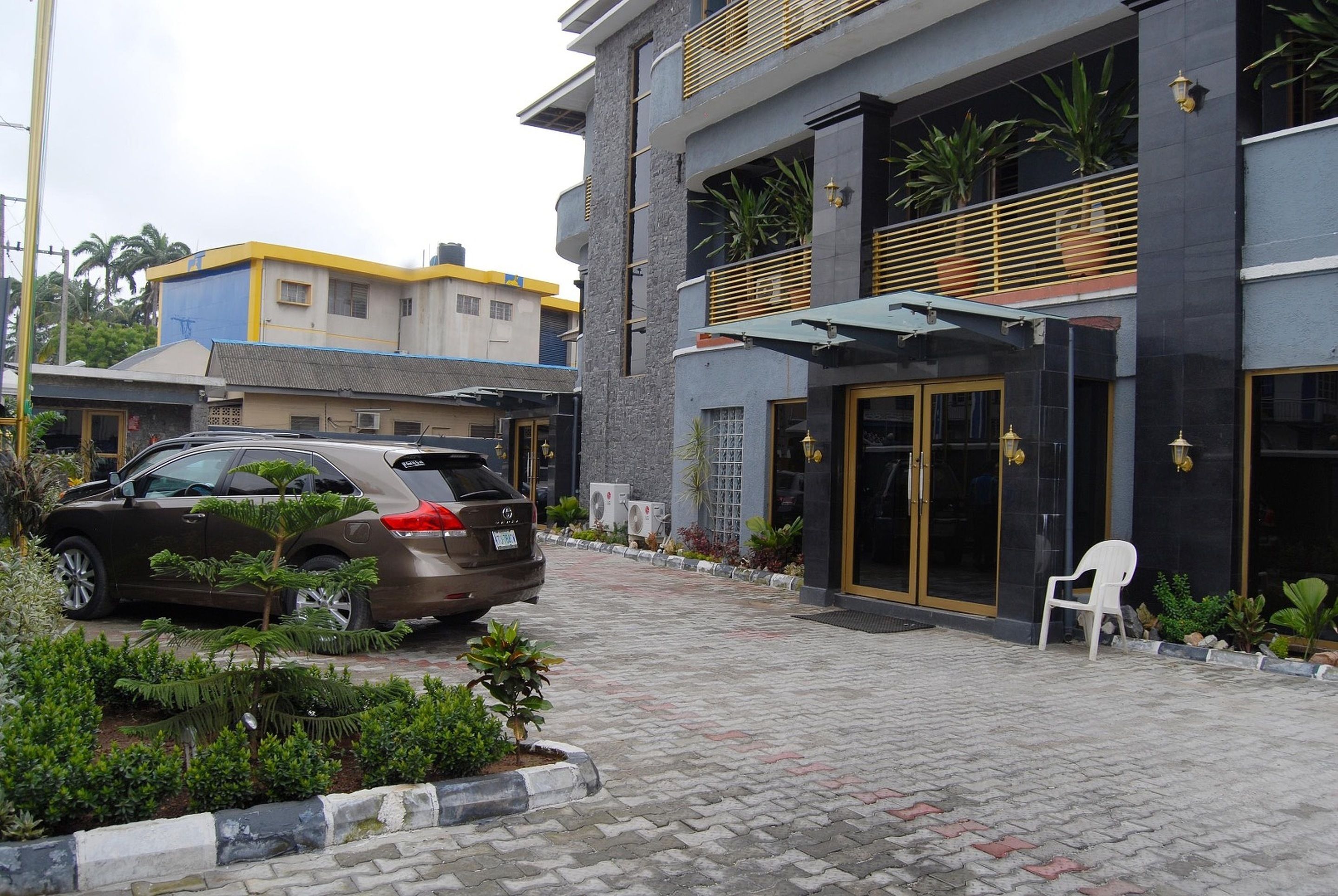 A modern building with a paved entrance, a parked SUV, and a white plastic chair.