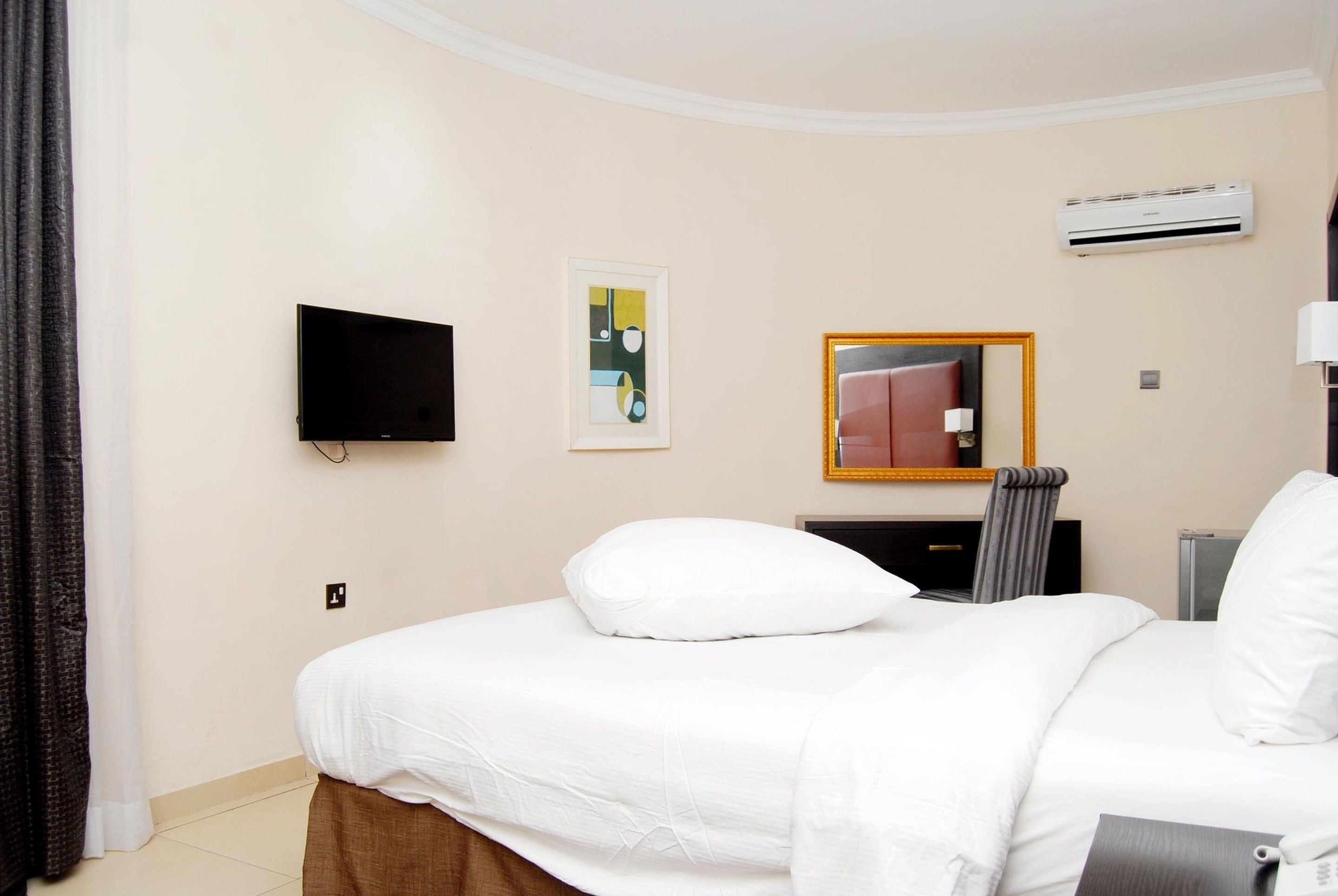 A hotel room with a bed, a flat-screen TV, a framed artwork, an air conditioning unit, and a mirror.