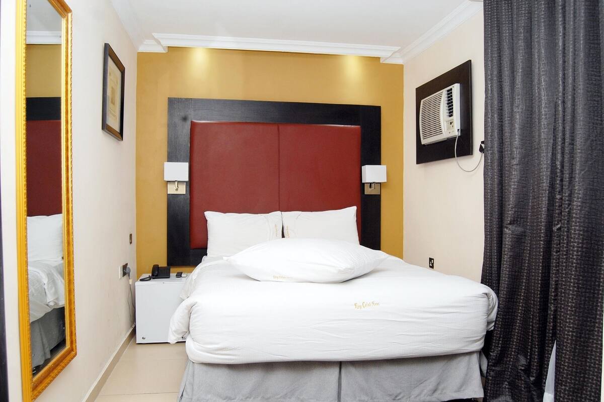A hotel room with a bed, bedside lamps, a wall-mounted air conditioner, and a mirror.