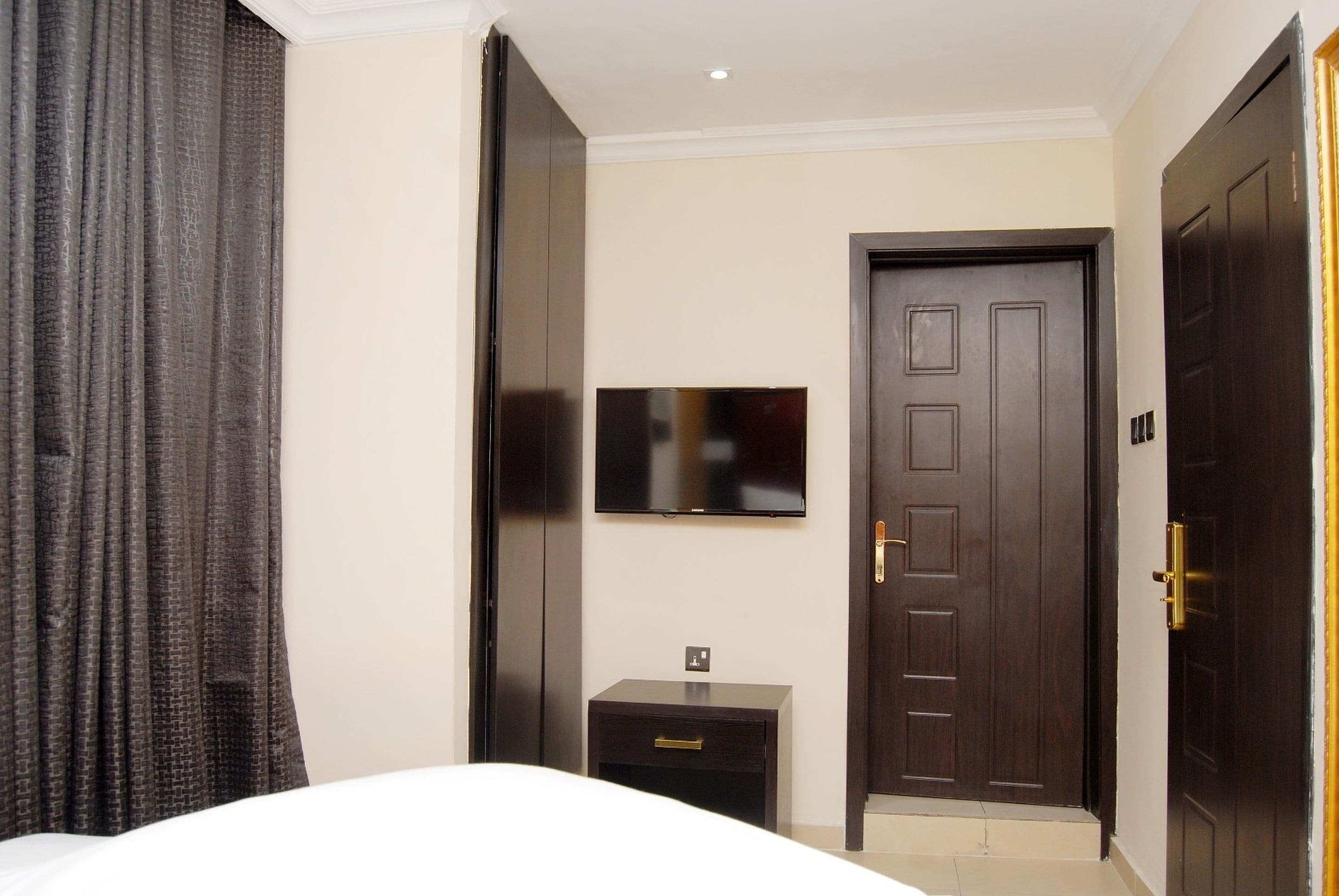A hotel room with a bed, a bedside table, a TV mounted on the wall, and a door.