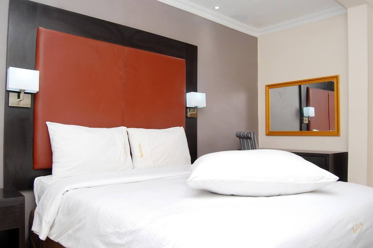 A hotel room with a large bed, two bedside lamps, a mirror, and a dark wooden headboard.