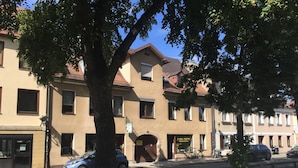 A row of beige buildings with a central entrance, a sidewalk, and parked cars.