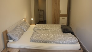 A bedroom with a bed, pillows, a nightstand, a dresser, and a mirror.