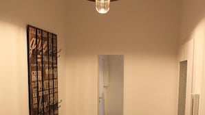 A hallway with a wooden floor, a hanging light fixture, a mirror, and a wall-mounted artwork.