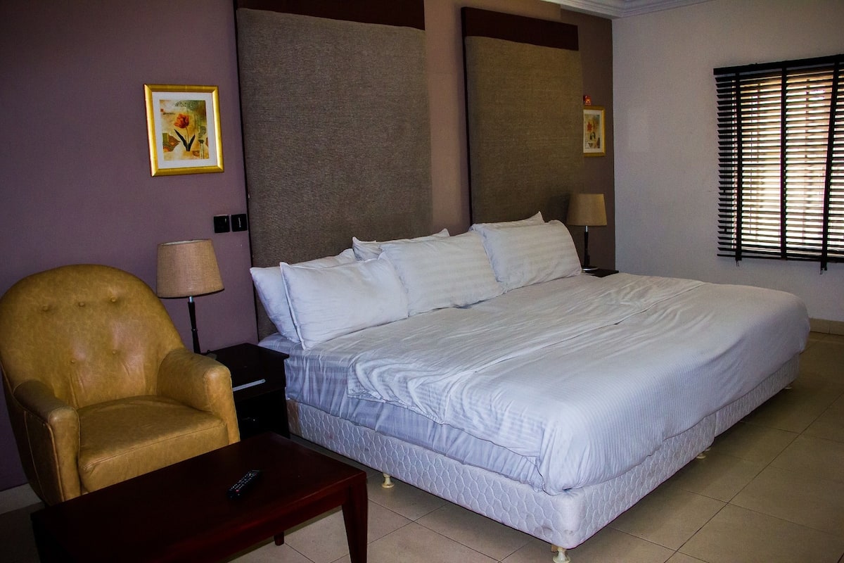 A hotel room with a large bed, a chair, a nightstand, and a lamp.