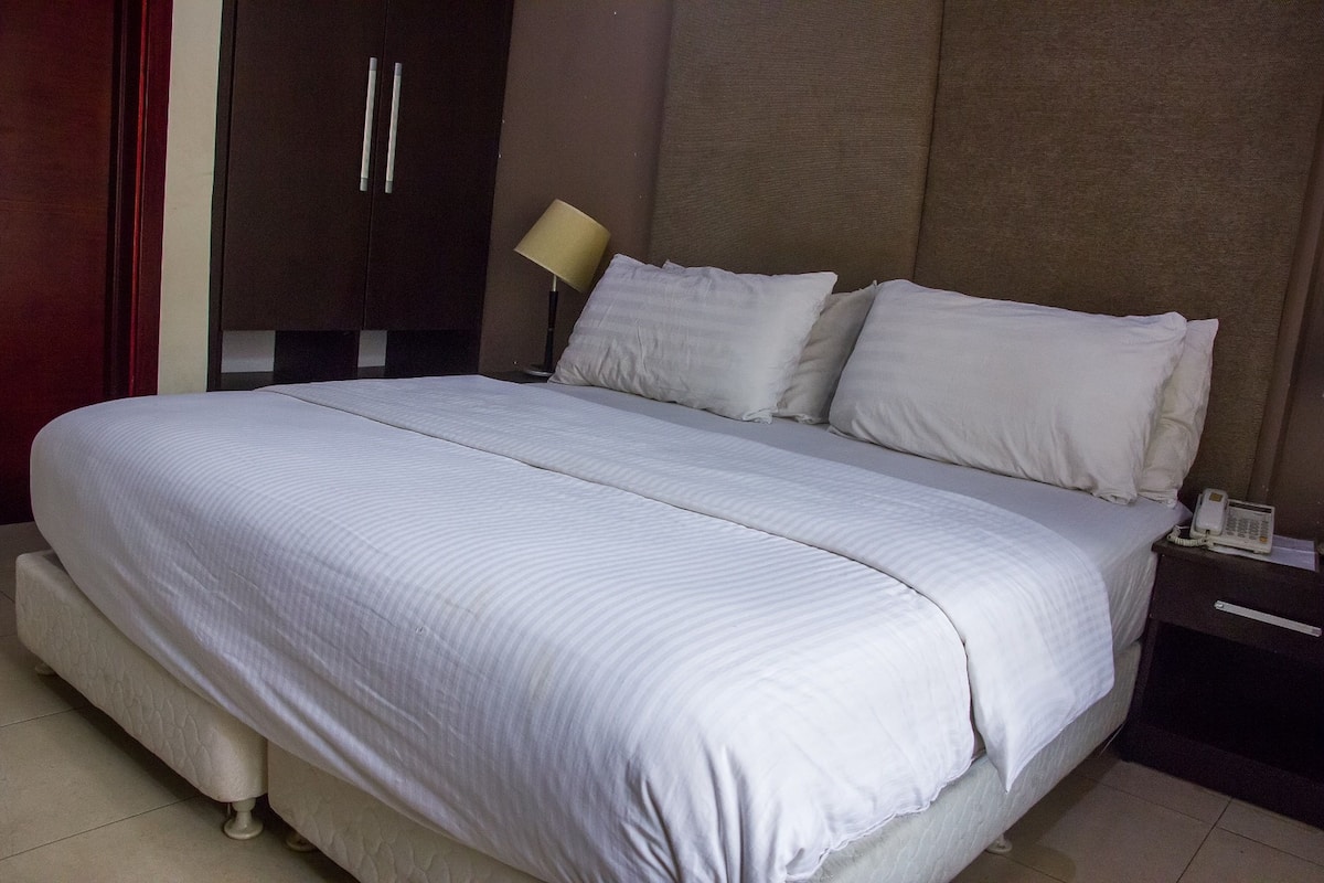 A large bed with a white bedspread and pillows, a bedside lamp, and a phone on the nightstand.
