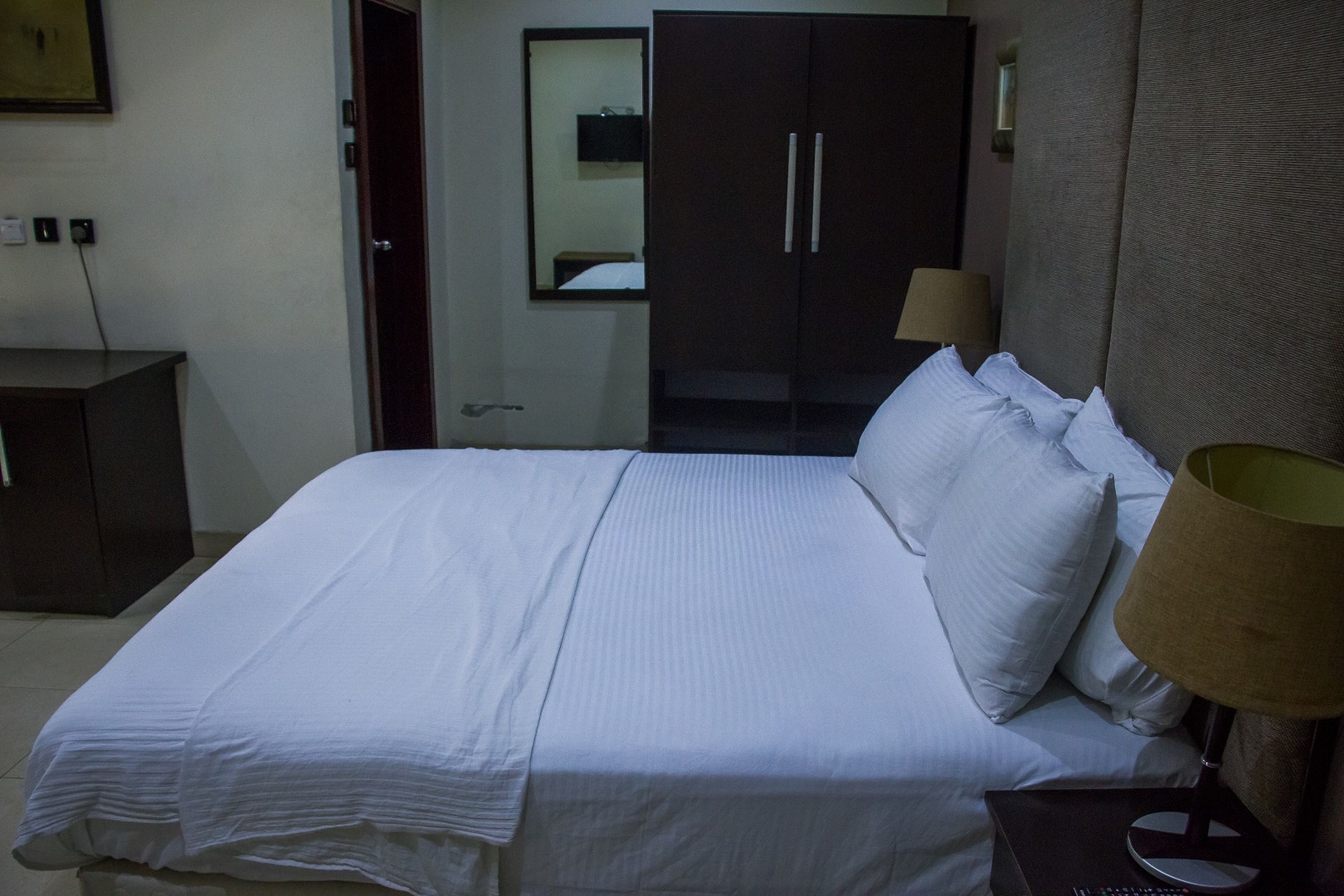 Una habitación de hotel con una cama, una mesita de noche, una lámpara, un armario y un espejo.