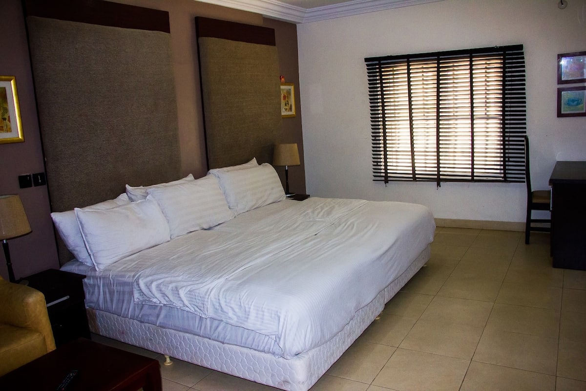 A neatly made bed in a hotel room with a large window and a lamp on the side.