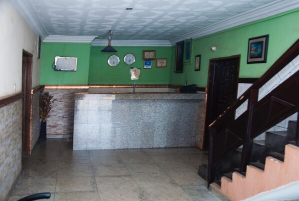 A lobby with a reception desk, a staircase, and a wall with clocks and framed certificates. - Alfoscar Hotel & Suites (Lagos)