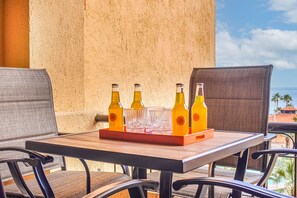 Ein Tisch mit Tablett, auf dem vier Flaschen und Gläser stehen, vor einer strukturierten Wand mit Blick auf das Meer und Palmen.