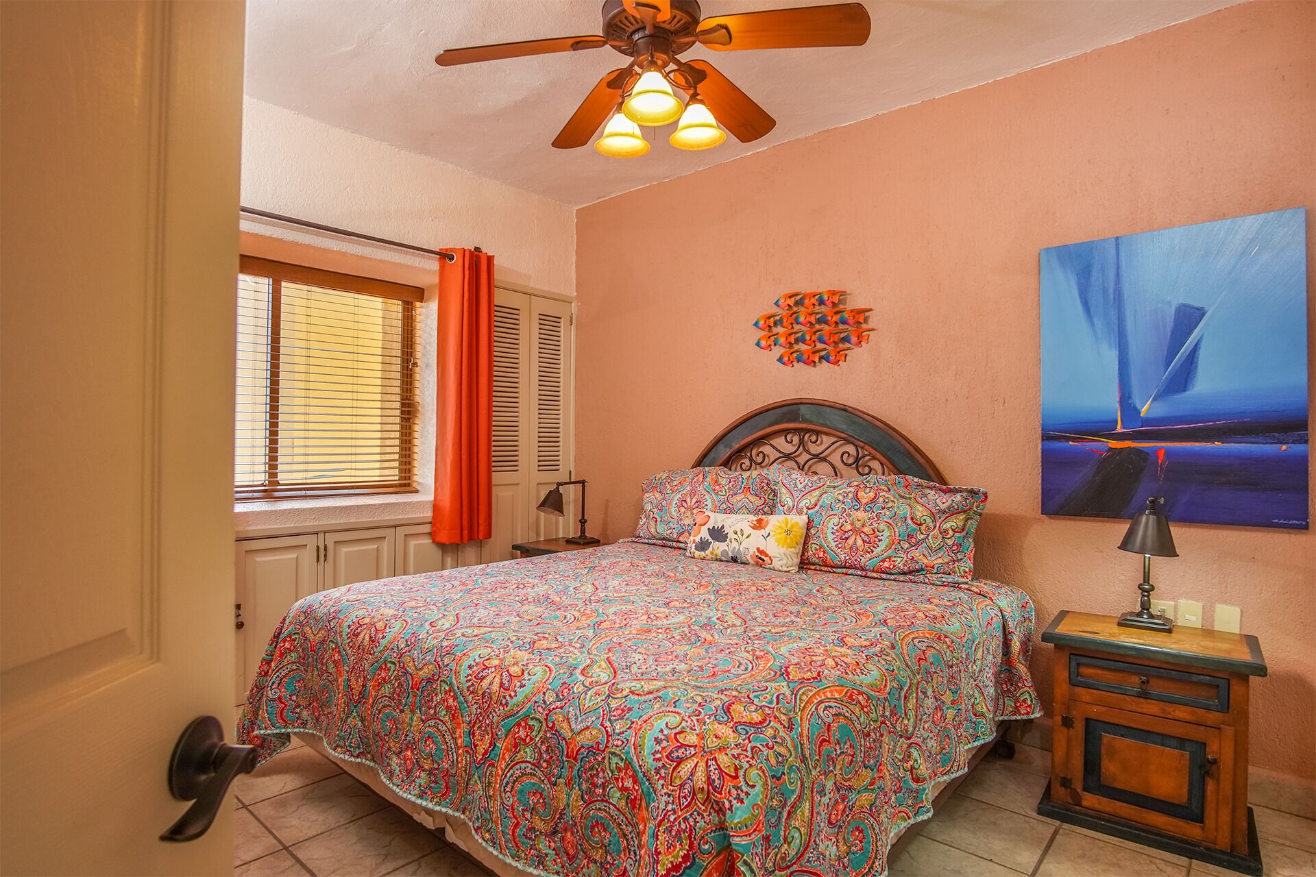 A bedroom with a bed, a nightstand, a ceiling fan, a window with blinds, and a painting on the wall.