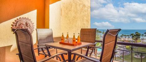 A balcony with a table set for two, featuring wicker chairs and a wooden table.