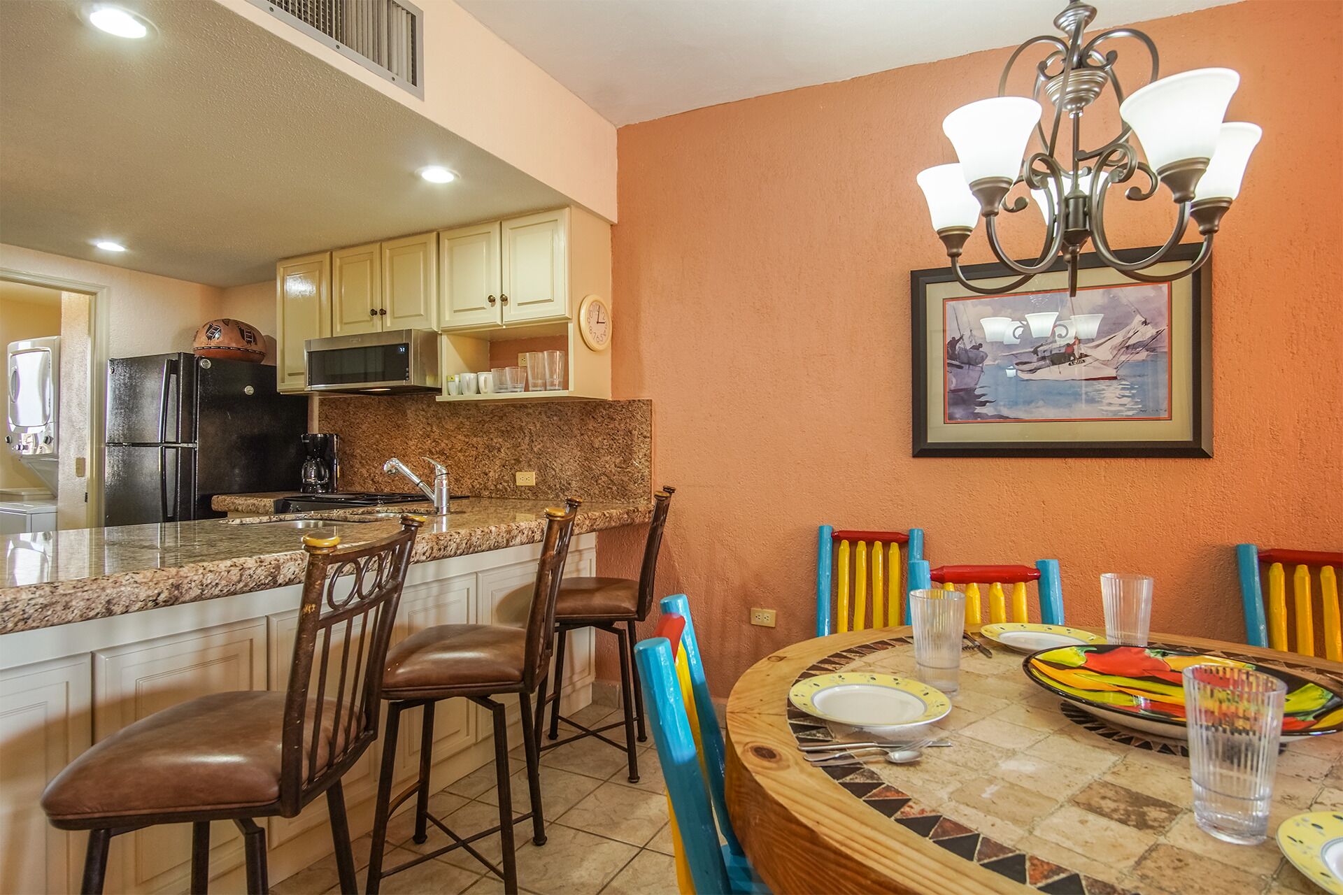 A kitchen with a granite countertop, a refrigerator, a microwave, and a dining area with a round table and chairs.
