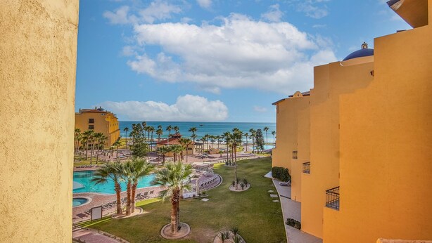 A resort with a pool, palm trees, and a view of the ocean. - C 401 Spacious Well Furnished Ocean View Condo (Puerto Peñasco)