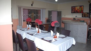 A dining area with tables set for four, each with a white tablecloth, vases with flowers, and chairs. - Bella Rose Hotel (Lagos)