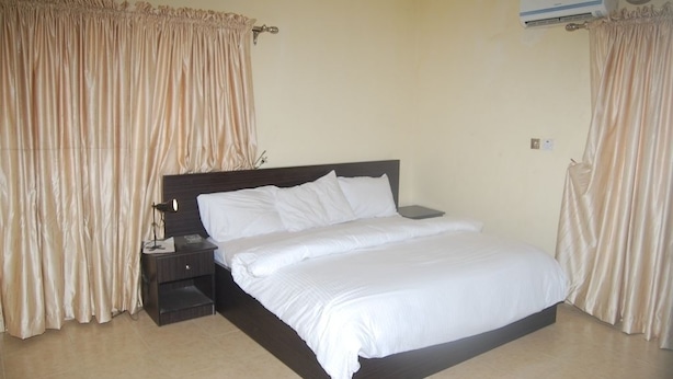 A bedroom with a large bed, a nightstand, and an air conditioning unit. - Bella Rose Hotel (Lagos)