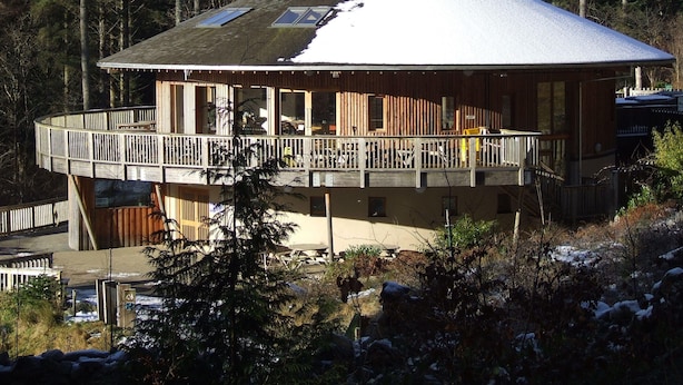A cabin with a wooden exterior, a balcony, and a snow-covered roof.