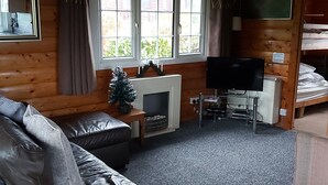 A cozy cabin interior with a leather sofa, a fireplace, a television, and a bunk bed.