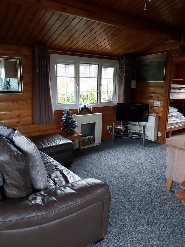 A cozy cabin interior with a leather sofa, a fireplace, a television, and a bunk bed.