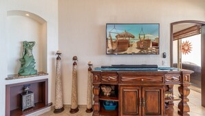Ett rum med ett skrivbord i trä, en tv som är monterad på väggen och dekorativa föremål, inklusive en staty och mönstrade pelare.