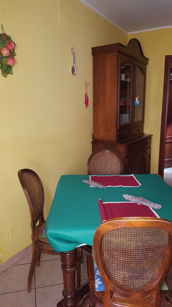 A dining area with a green tablecloth, wooden chairs, a wooden cabinet, and a wall-mounted decoration. - The house of the lodole (Monreale)