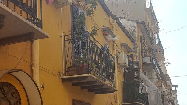 Een geel gebouw met een houten deur en een balkon met bloempotten.