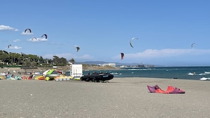 A beach with multiple kites flying, a lifeguard tower, and a few beachgoers. - Park Beach: Ground floor apartment, garden, nxt to pool, nr beach. Free parking (ESTEPONA  MALAGA)