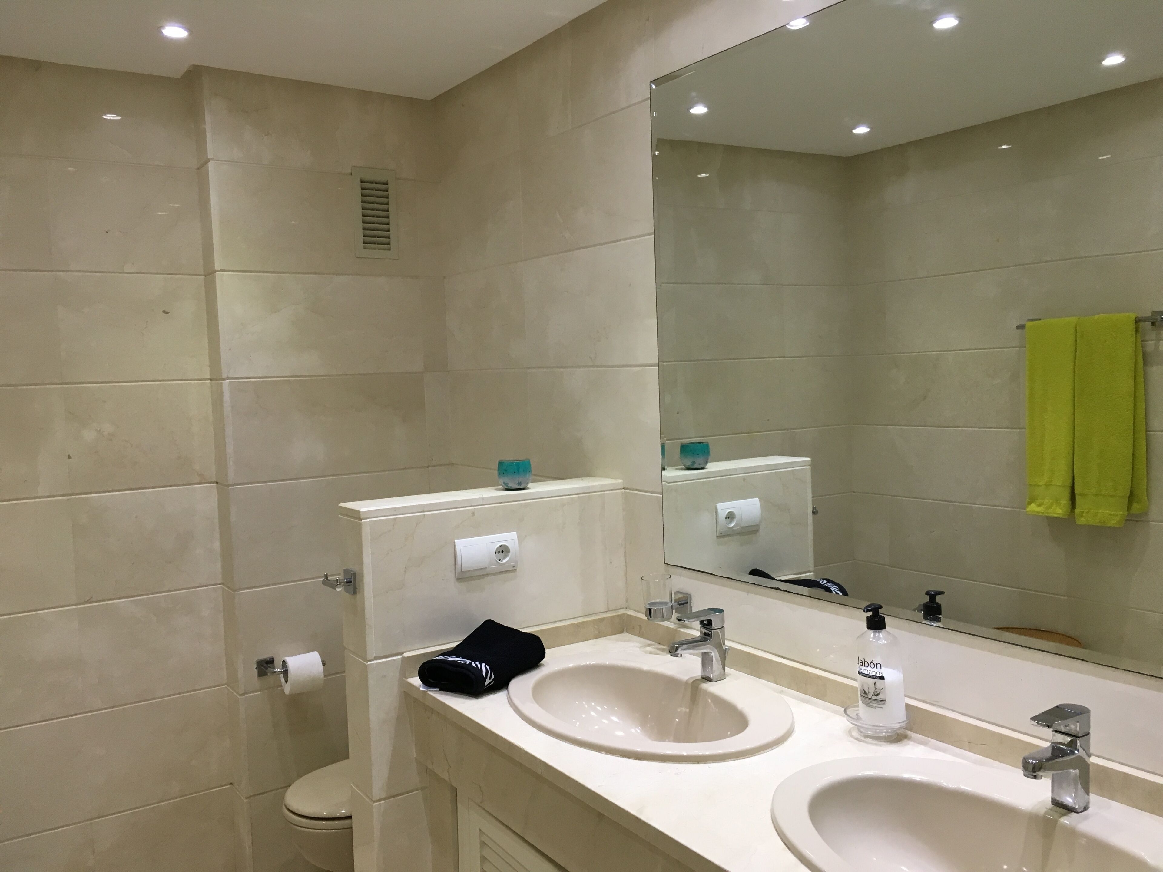 Een badkamer met twee wastafels, een toilet, een spiegel en een handdoekhouder met een groene handdoek.