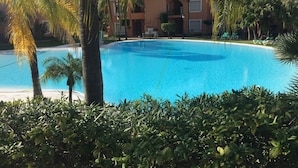 A large, clear swimming pool surrounded by lush greenery and a multi-story building with balconies. - Park Beach: Ground floor apartment, garden, nxt to pool, nr beach. Free parking (ESTEPONA  MALAGA)