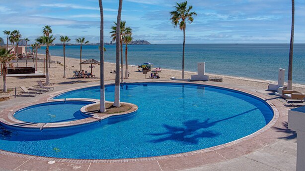 Ein Swimmingpool mit Palmen, einem Strand und Blick aufs Meer.