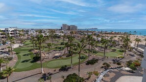 Ein Golfplatz mit Palmen, einem Strand und Gebäuden im Hintergrund.