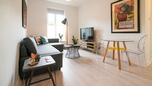 A modern living room with a sofa, a coffee table, a TV, and a dining table with chairs. - Stylish boutique apartment in trendy West Didsbury (Manchester)