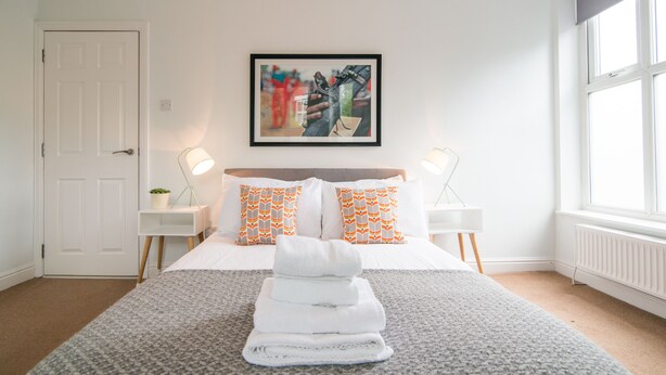 A hotel room with a neatly made bed, a framed artwork on the wall, and a window providing natural light. - Stylish boutique apartment in trendy West Didsbury (Manchester)