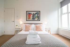 A hotel room with a neatly made bed, a framed artwork on the wall, and a window providing natural light. - Stylish boutique apartment in trendy West Didsbury (Manchester)