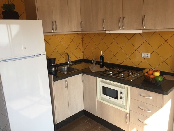 Una cocina compacta con armarios de madera, un microondas integrado, una estufa a gas y un lavamanos.