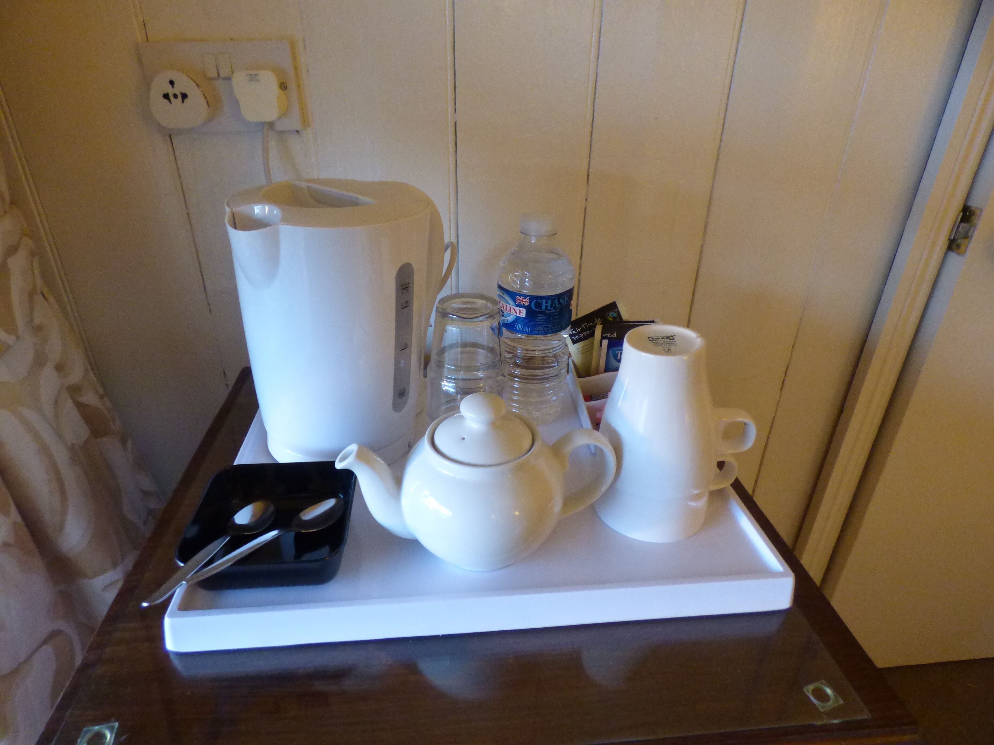 Una bandeja con tetera, hervidor, tazas, botella de agua y un recipiente pequeño con cubiertos.