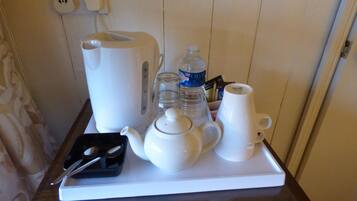 Una bandeja con tetera, hervidor, tazas, botella de agua y un recipiente pequeño con cubiertos.