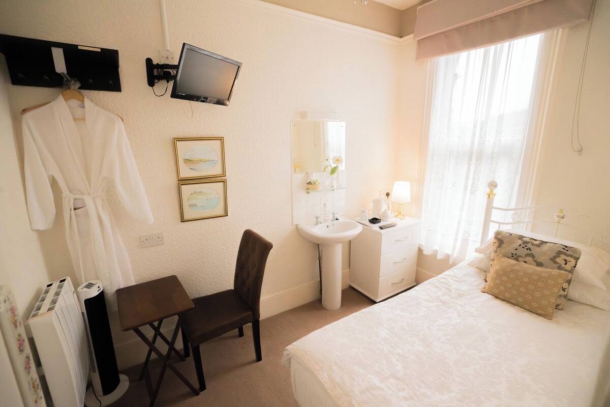 A hotel room with a bed, a desk, a chair, a TV, a sink, and a window with curtains.
