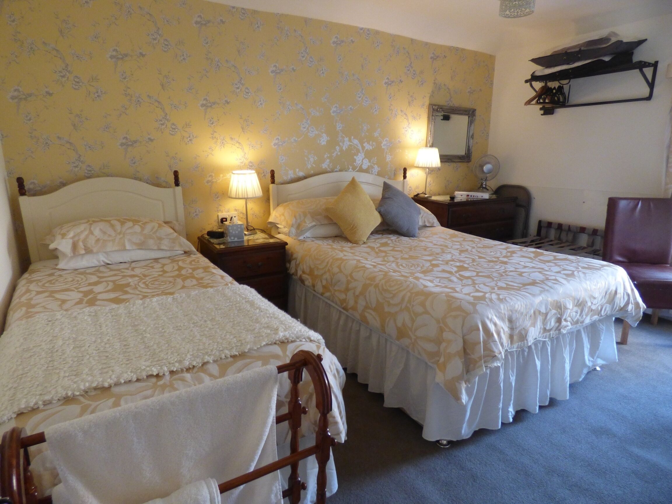 A hotel room with two single beds, a wooden chair, a nightstand with a lamp, and a mirror on the wall.