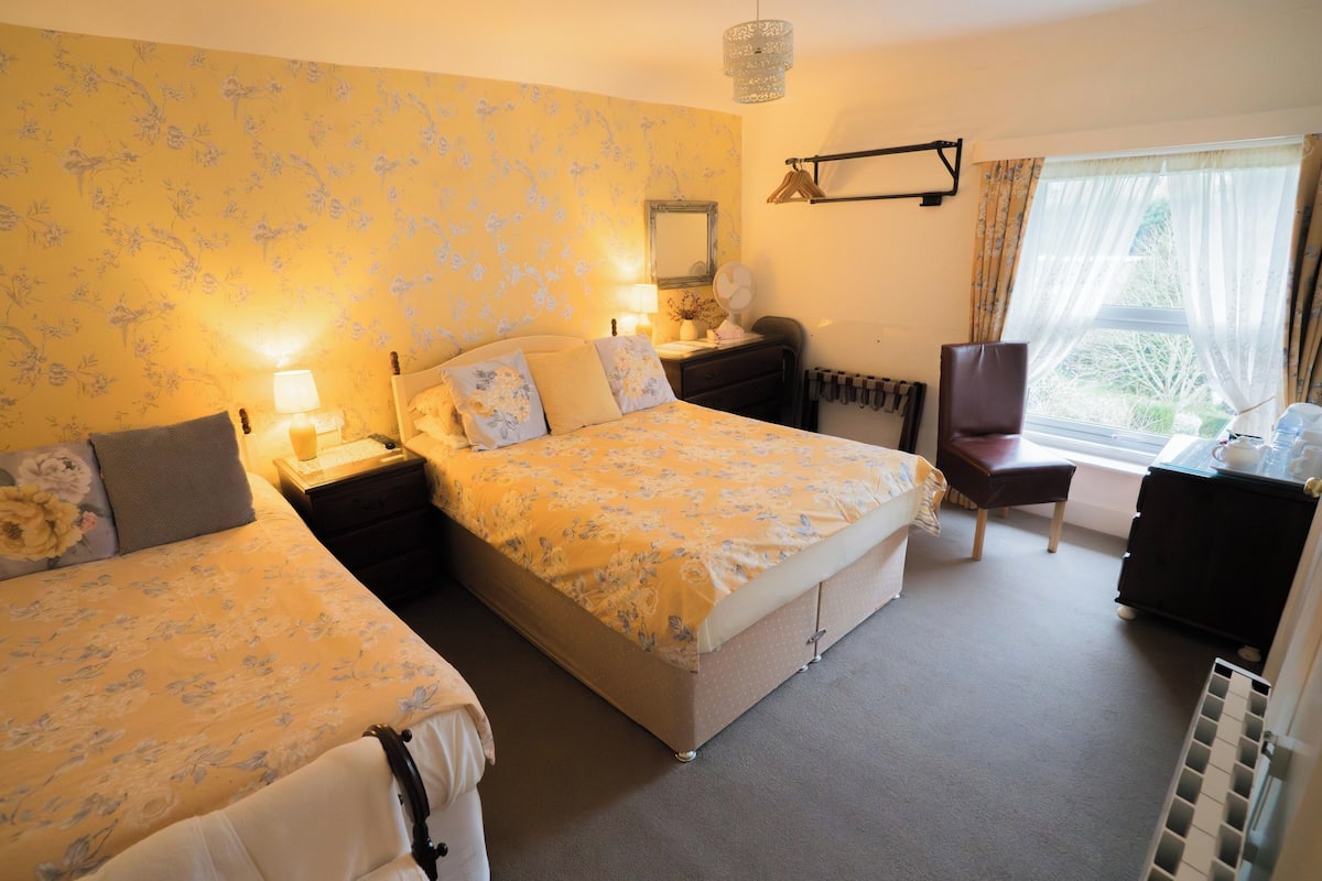 A hotel room with two beds, a chair, a desk, a mirror, and a window with curtains.