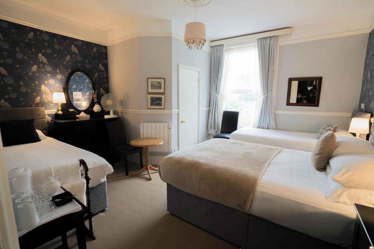 A hotel room with two beds, a desk with a lamp, a chair, a mirror, and a window with curtains.