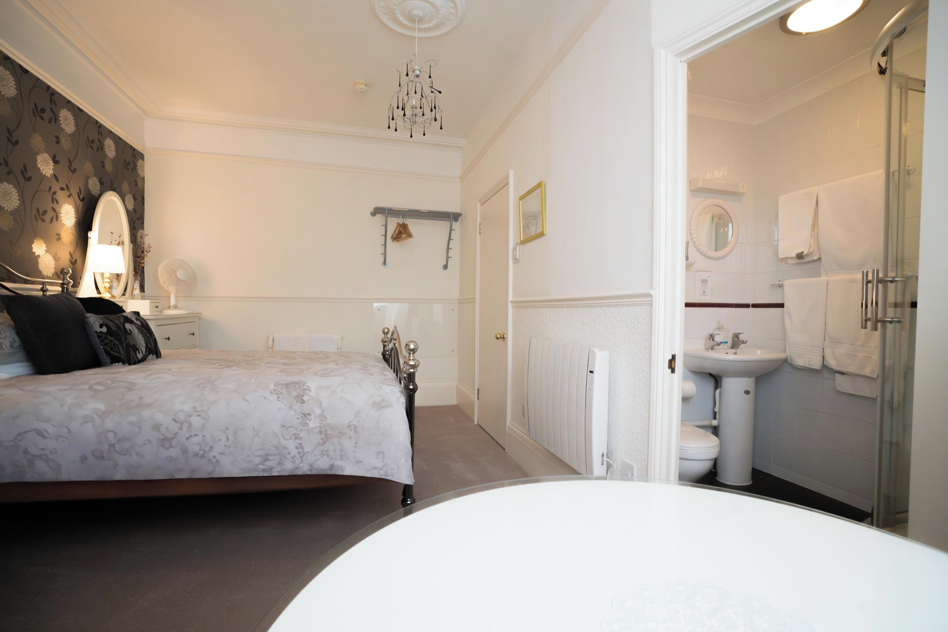 A bedroom with a bed, bedside table, and a nightstand. There is a bathroom with a sink, mirror, and towel rack.