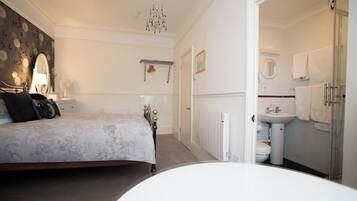 A bedroom with a bed, bedside table, and a nightstand. There is a bathroom with a sink, mirror, and towel rack.