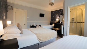 A hotel room with two beds, a TV, a mirror, a shower, and a small table with a lamp. - Maison Dieu Guest House (Dover)