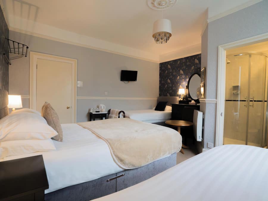 A hotel room with two beds, a TV, a mirror, a shower, and a small table with a lamp.