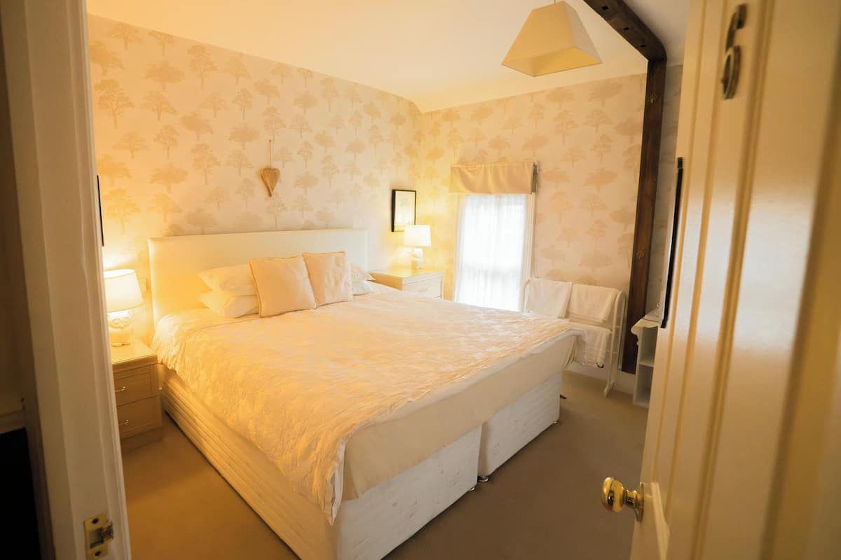 A neatly arranged bedroom with a large bed, bedside tables, and a window with curtains.