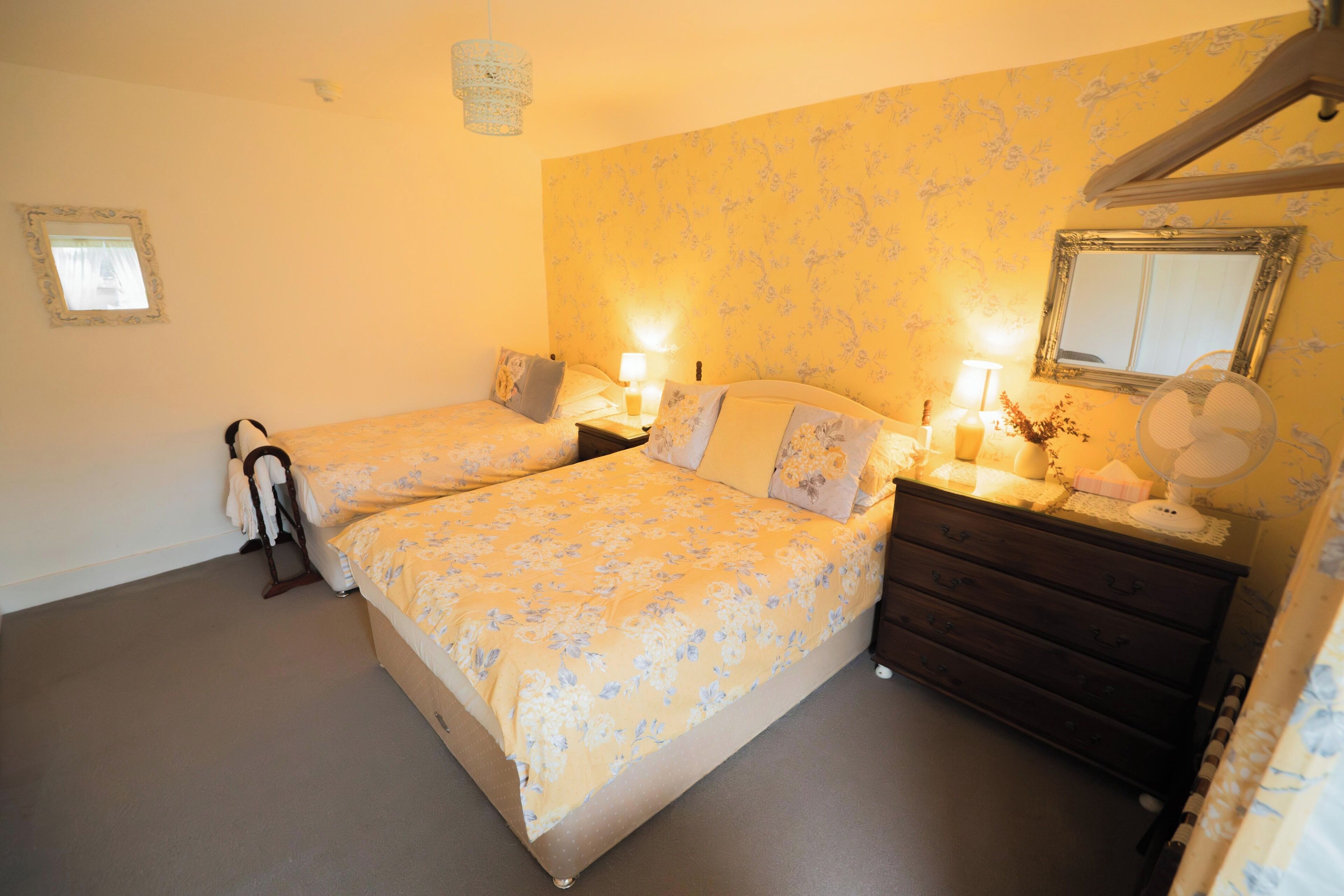A bedroom with two beds, a dresser, a mirror, and a small window.
