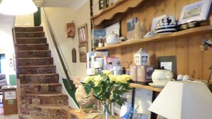A staircase with patterned carpet leading to a wooden staircase. A wooden cabinet with drawers and a vase of yellow flowers is on the landing. - Maison Dieu Guest House (Dover)